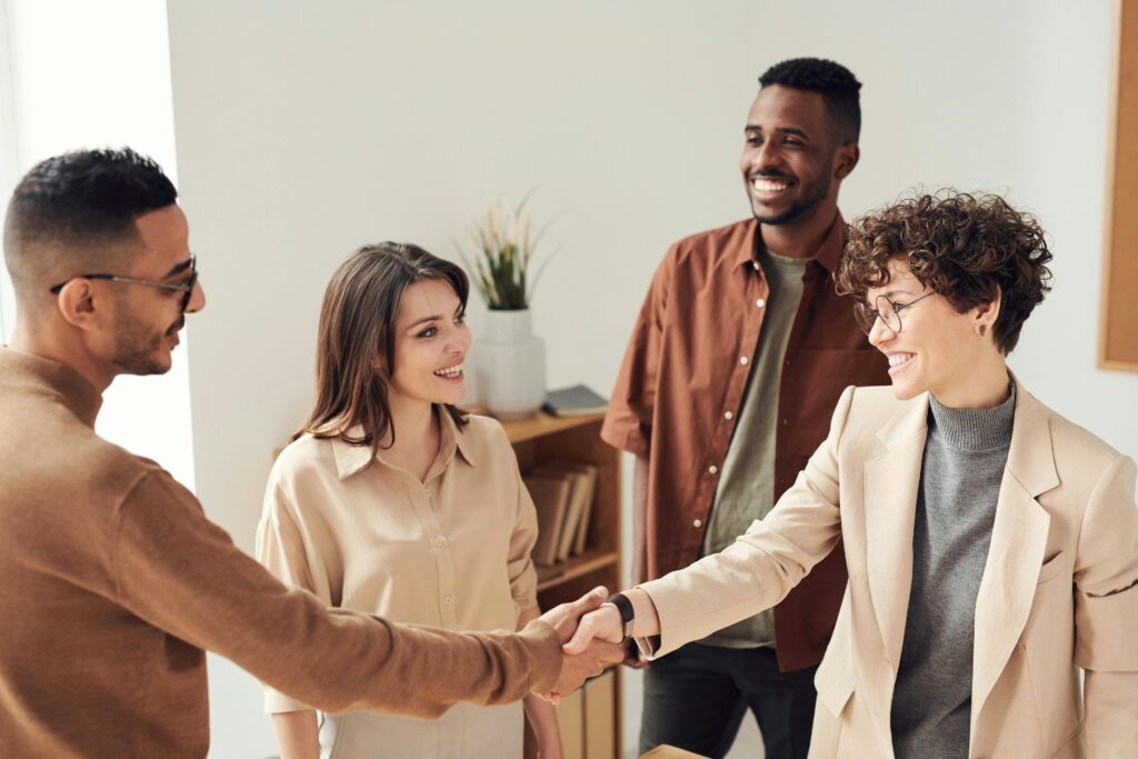 pexels-photo-3184416-3184416 Four colleagues smiling and shaking hands in a bright office setting.